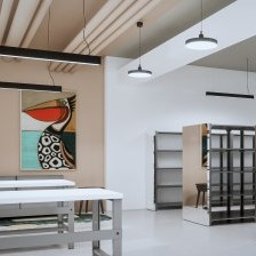 MERIDIAN EU Sp. z o. o. - Nowoczesne wnętrze showroomu z beżową ścianą, na której wisi duży, kolorowy obraz pelikana. Sufit z widocznymi instalacjami i minimalistycznym oświetleniem liniowym, długie stoły.