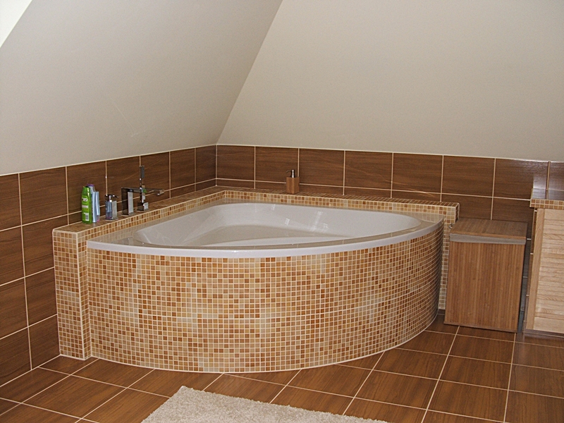 Narożna wanna obłożona mozaiką w odcieniach brązu w łazience na poddaszu, z brązowymi płytkami na ścianach i podłodze, uzupełniona o drewniane szafki.