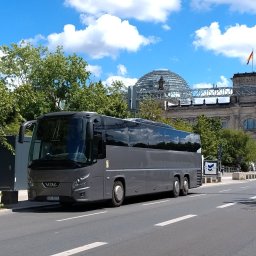 Baltic TRAVEL - Szary autokar VDL z przyciemnianymi szybami, zaparkowany na ulicy przed historycznym budynkiem Reichstagu ze szklaną kopułą i niemiecką flagą, w słoneczny dzień.