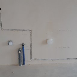Elektro-Smart - Ściana z częściowo ułożoną instalacją elektryczną w rurkach i rurami wodno-kanalizacyjnymi, z odręcznymi oznaczeniami wymiarów i przeznaczenia, np. 'koniec brodzik'.