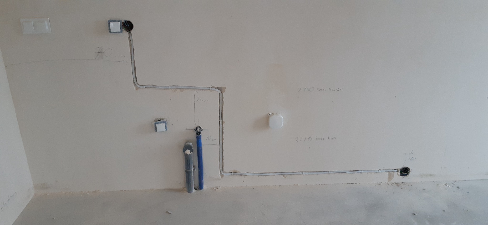Ściana z częściowo ułożoną instalacją elektryczną w rurkach i rurami wodno-kanalizacyjnymi, z odręcznymi oznaczeniami wymiarów i przeznaczenia, np. 'koniec brodzik'.