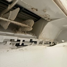KlimFaktor - Mocno zakurzone wnętrze jednostki klimatyzacyjnej z widocznymi brudnymi łopatkami wentylatora i kratkami, wskazujące na potrzebę czyszczenia.