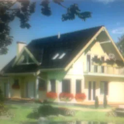 Dwukondygnacyjny dom z poddaszem użytkowym, kremową elewacją, ciemnym dachem, oknami dachowymi i balkonem z kwiatami, widoczny z perspektywy ogrodu z elementami wodnymi.