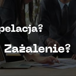 Kancelaria Adwokacka adw. dr Kamil Bajer - Trzy osoby w strojach biznesowych pochylone nad dokumentami i laptopem na stole, z dłońmi wskazującymi na papiery. Widoczny tekst 'Apelacja? Zażalenie?' w biurowym otoczeniu.