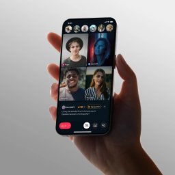 Slash Dot Filip Radomski - Dłoń trzymająca nowoczesny smartfon z aktywną wideorozmową grupową, prezentującą cztery osoby i sekcję czatu z pytaniem o naukę gry na instrumencie.