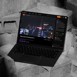 Slash Dot Filip Radomski - Czarny laptop na tle szarych, surowych betonowych bloków, wyświetlający platformę Trading.TV z wykresem Bitcoina, prelegentem i czatem na żywo o handlu kryptowalutami.