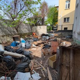 As Serwis - Obszerny stos gruzu budowlanego, połamanych mebli, drewna, płytek i czarnych worków na śmieci, zalegający na podwórku przy żółtym budynku i betonowym murze.