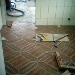 Układanie brązowej, wzorzystej terakoty w łazience, widoczne narzędzia glazurnicze i odkurzacz przemysłowy, płytki ułożone do połowy pomieszczenia.