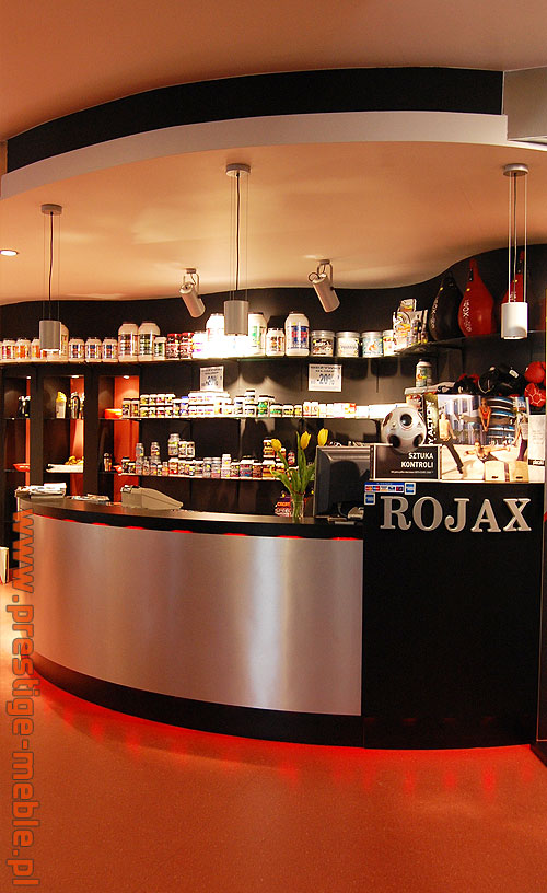 Recepcja sklepu z suplementami diety z półkami pełnymi produktów, oświetleniem punktowym i podświetleniem LED u dołu lady.