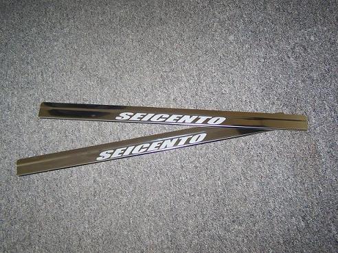 Dwie nakładki progowe z napisem SEICENTO, ułożone ukośnie na szarym, teksturowanym tle.