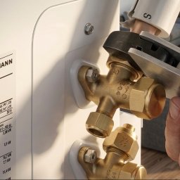 Domgard - Instalacje Optymalne - Instalacja mosiężnych zaworów na białej jednostce Viessmann, gdzie dłonie technika precyzyjnie dokręcają złączki specjalistycznym narzędziem.