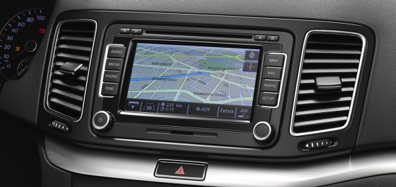 Wnętrze samochodu z widocznym systemem nawigacji GPS z mapą ulic miasta na ekranie dotykowym, kratki wentylacyjne po bokach i panel sterowania klimatyzacją poniżej.