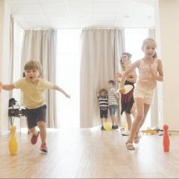 Holimo Hotel Restauracja & SPA - Rozbiegane dzieci grające w kręgle w jasnej, przestronnej sali z drewnianą podłogą, pod nadzorem animatora w Stroniu Śląskim.