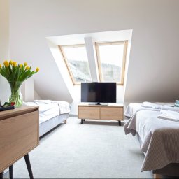 Holimo Hotel Restauracja & SPA - Przytulny pokój na poddaszu z dwoma pojedynczymi łóżkami, telewizorem pod oknami dachowymi, drewnianą szafką nocną z żółtymi tulipanami i zestawem do kawy.