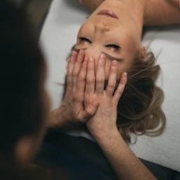 Centrum medyczne VitMeUp Wrocław - Kobieta w różowym topie leży na leżance, a dłonie terapeuty delikatnie zakrywają jej oczy podczas zabiegu na twarz, skupiając się na relaksie.