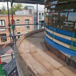 BIST BUILDERS - Zakrzywiona konstrukcja pokryta zielonymi, błyszczącymi płytkami ceramicznymi, częściowo ułożonymi na niebieskiej izolacji. Widoczne drewniane deskowanie i rusztowanie budowlane.