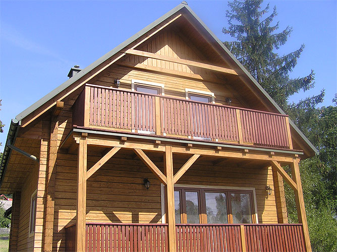 Dwukondygnacyjny dom z drewna, z balkonami na obu poziomach, wykończony w naturalnym kolorze drewna z ciemniejszymi balustradami, uchwycony w słoneczny dzień.