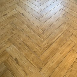 Poznań Remonty - Wykończenia Wnętrz KS BUD - Jasna podłoga z drewnopodobnych paneli lub płytek, ułożona w klasyczny wzór jodełki, z widoczną strukturą drewna i delikatnym połyskiem odbijającym światło.
