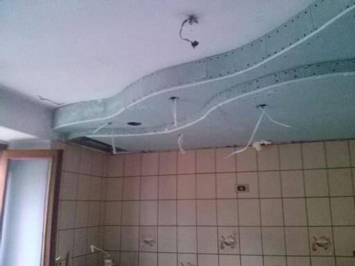 Nieregularny sufit podwieszany z płyt kartonowo-gipsowych w trakcie montażu, widoczne przewody elektryczne i płytki na ścianach.