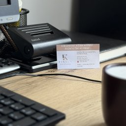 Biuro rachunkowe Finkey - Wizytówka biura rachunkowego Finkey z hasłem 'Wspieramy rozwój Twojej firmy' i ofertą darmowej konsultacji, leżąca na drewnianym biurku obok dziurkacza Eagle, fragmentu klawiatury i kubka.