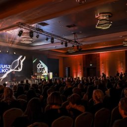 Gremium - Realizacja Techniczna i Studio Nagrań - Koncert Mateusza Ziółko w dużej sali, z artystą przy pianinie na scenie z ekranem LED i publicznością. Dynamiczne światła sceniczne rzucają wzory na sufit, tworząc uroczystą atmosferę wydarzenia.