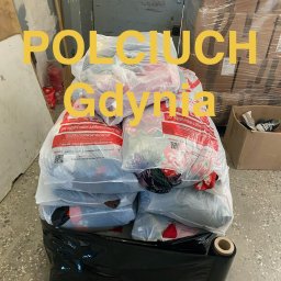 POLCIUCH Hurtownia Odzieży Używanej - Stos białych worków z czerwonymi napisami, częściowo owiniętych czarną folią stretch, na drewnianej palecie w magazynie. Na zdjęciu widoczny napis 'POLCIUCH Gdynia'.