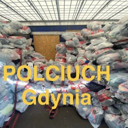 POLCIUCH Hurtownia Odzieży Używanej - Wnętrze ciężarówki wypełnione po brzegi przezroczystymi workami z odzieżą używaną, zabezpieczonymi pasami. W tle drewniany panel i siatka. Na pierwszym planie żółty napis 'POLCIUCH Gdynia'.