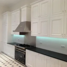 Nowoczesna kuchnia z białymi szafkami z frezowanymi frontami, czarnymi blatami i dużą, stylową, czarną kuchenką z mosiężnymi detalami.