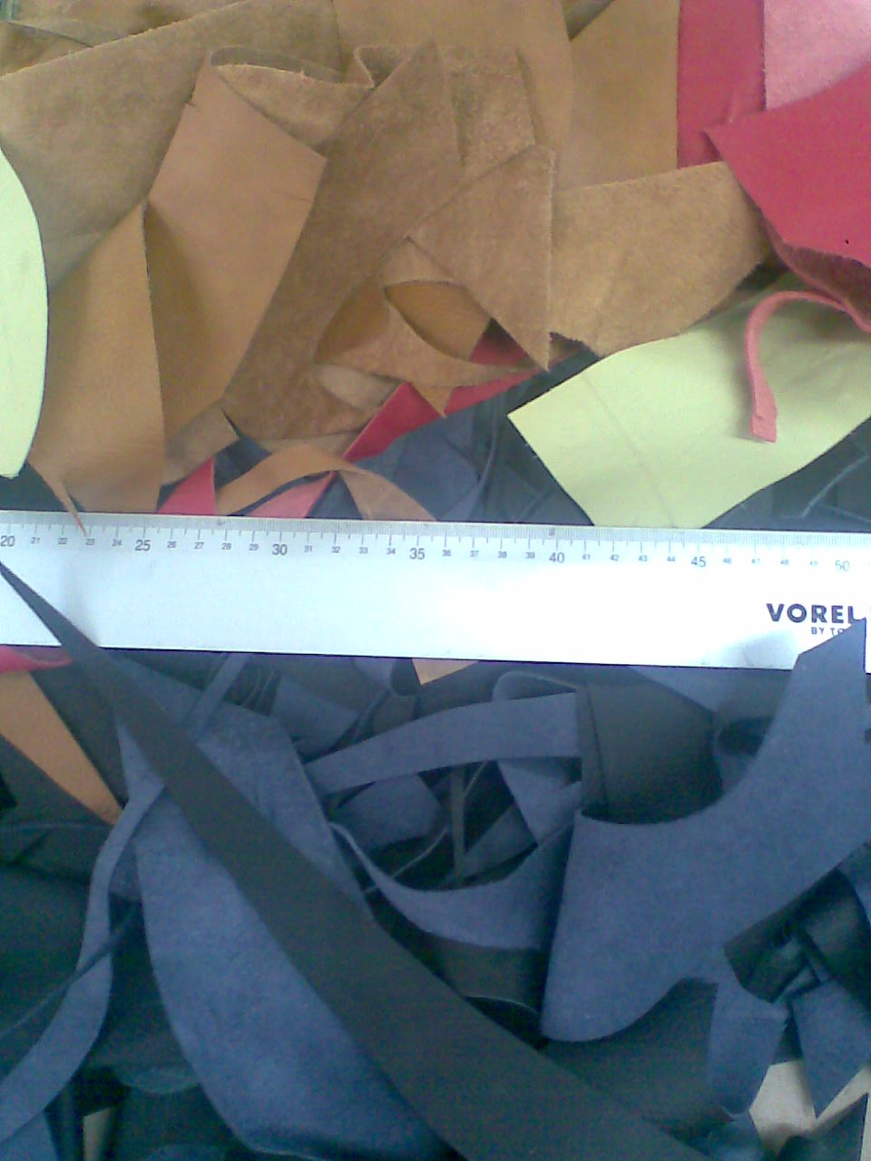 Ścinki różnych kolorów i faktur skór ułożone warstwami, z widoczną miarką Vorel dla skali.