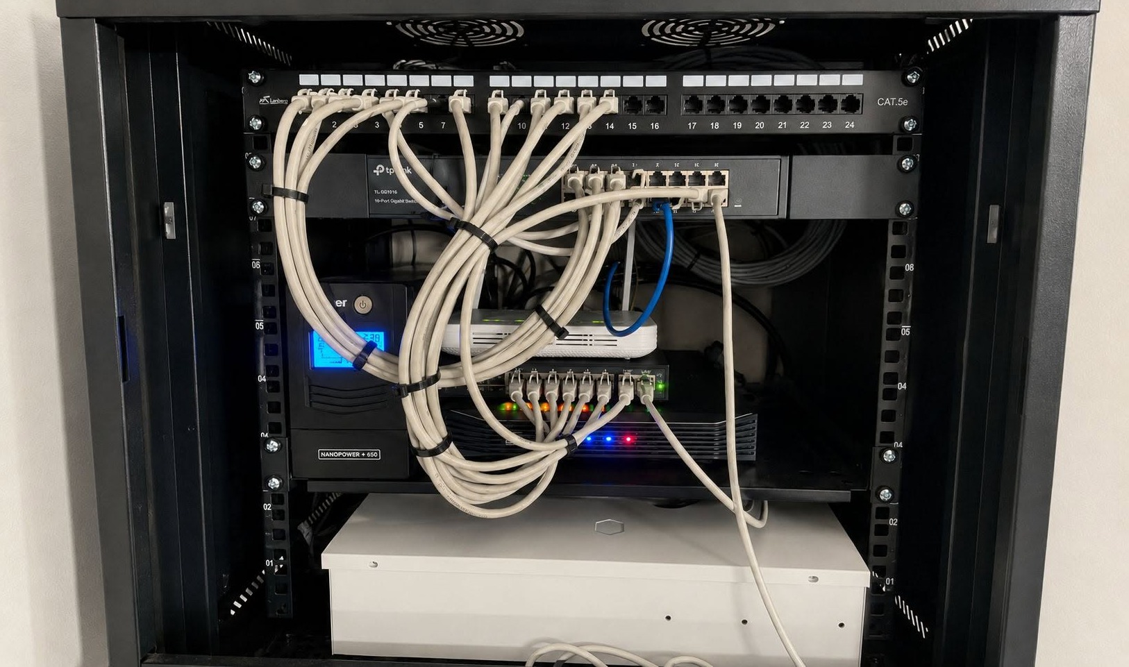 Profesjonalnie zainstalowana szafa rack z panelem krosowym CAT.5e, switchem TP-Link, UPS-em NANOPOWER i routerem, z uporządkowanym okablowaniem.