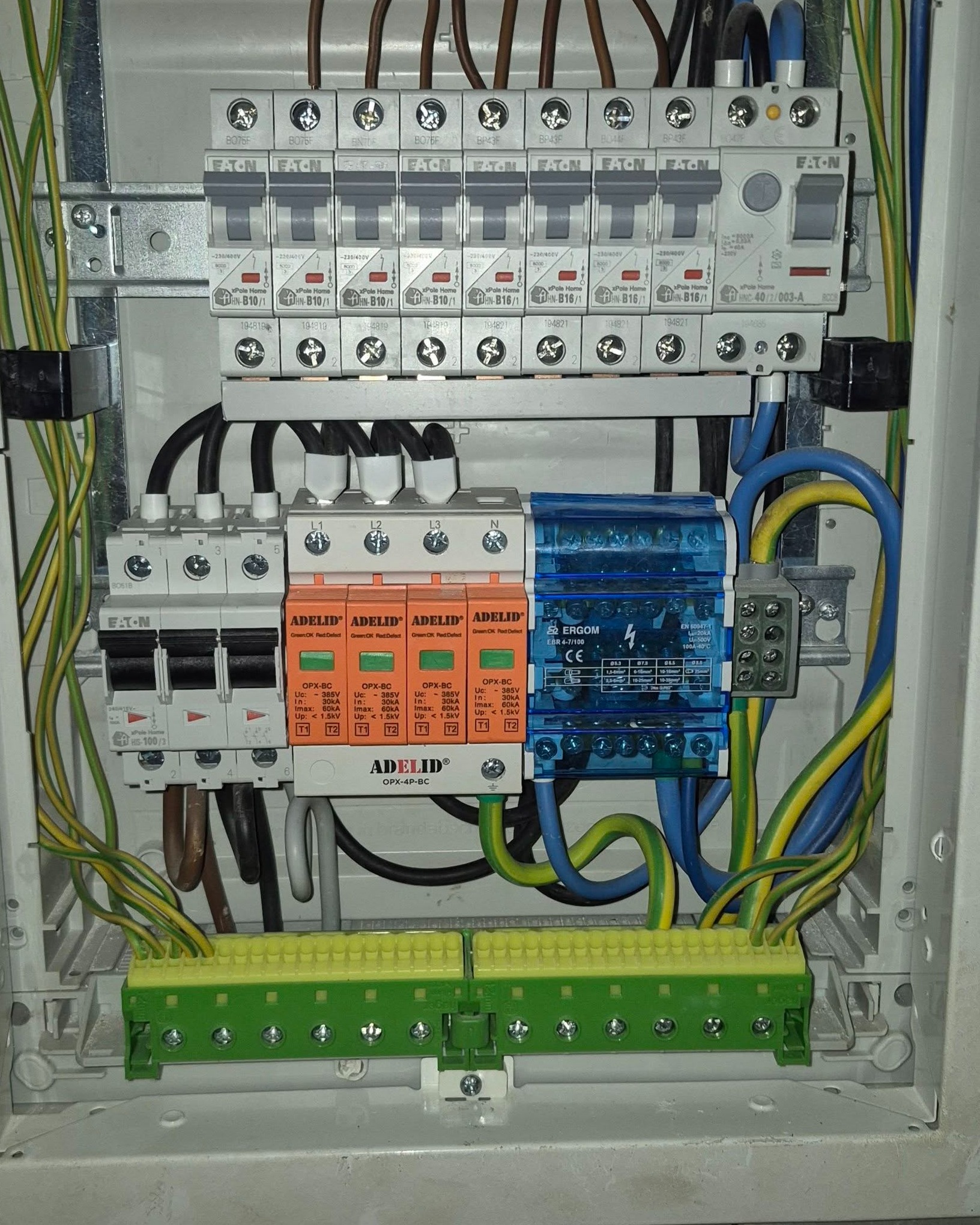 Wnętrze nowoczesnej rozdzielnicy elektrycznej z zamontowanymi wyłącznikami nadprądowymi EATON, ochronnikami przepięć ADELID i modułem ERGOM, z widocznym uporządkowanym okablowaniem.
