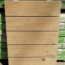 Centrum Drzewne Lucjan Huczek - Drewniana konstrukcja z desek, jasne drewno z widocznymi śrubami, na tle opakowań z zielonym nadrukiem, prosta forma, naturalny materiał.