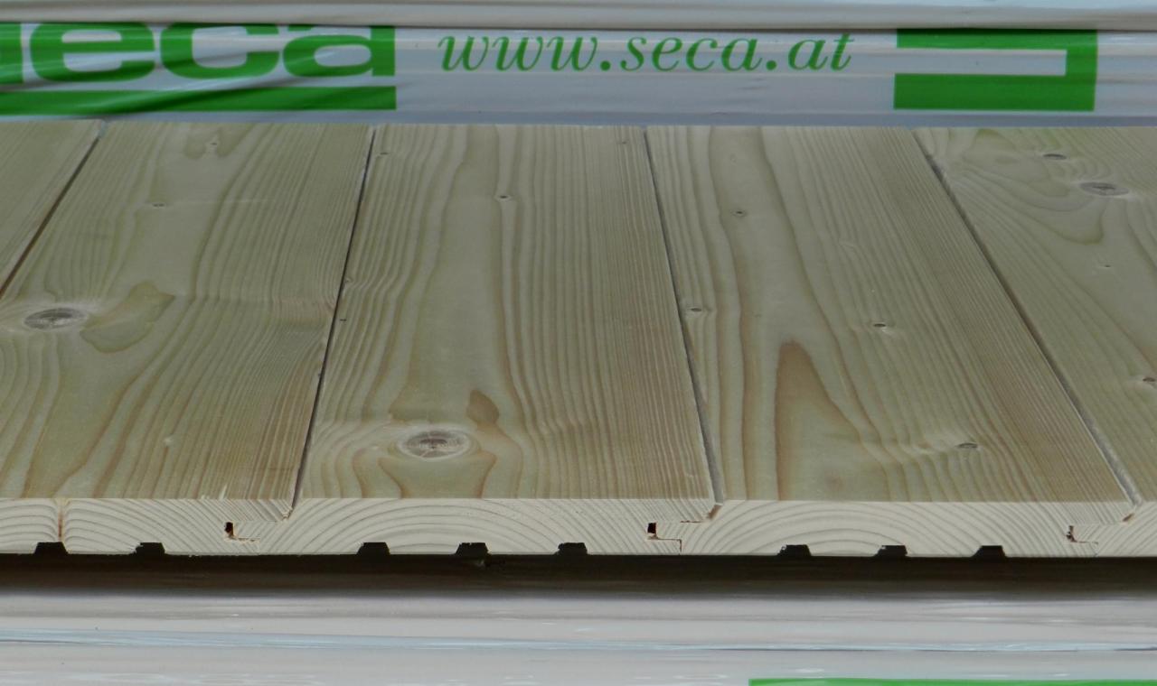 Jasne, heblowane deski podłogowe z widocznym profilem pióro-wpust, ułożone równolegle. W tle zielony nadruk z adresem strony internetowej.