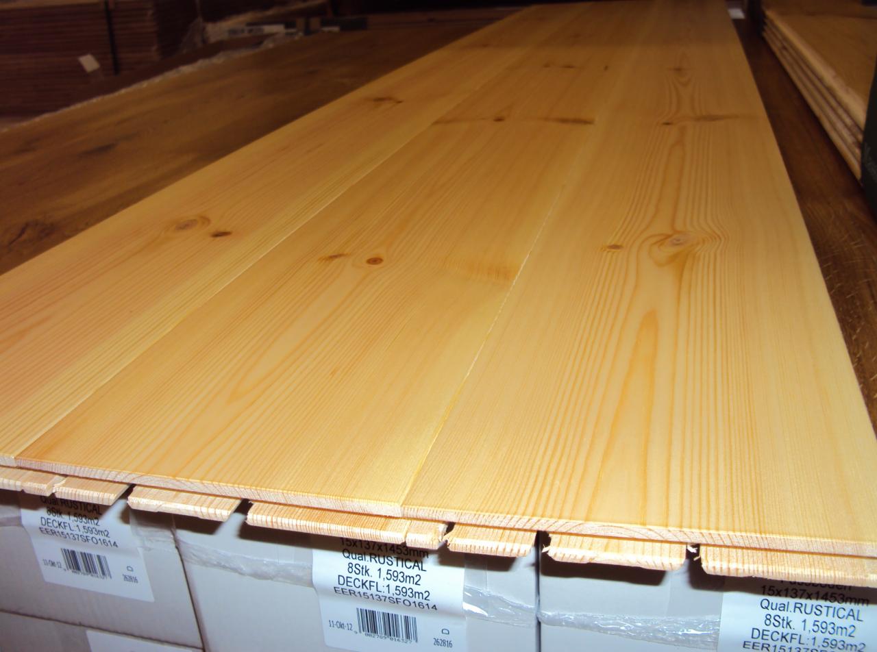 Jasne deski podłogowe z widocznym rysunkiem drewna, ułożone na opakowaniach z informacją o produkcie. Widoczne sęki i naturalna kolorystyka drewna.