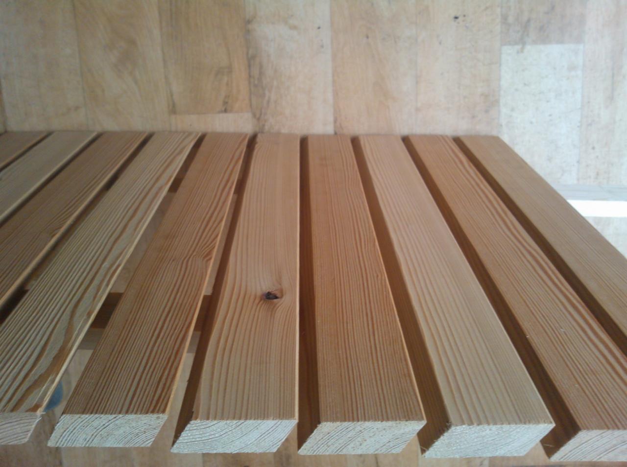 Jasne, świerkowe deski ułożone równolegle, widoczne słoje drewna i drobne sęki, w tle drewniana podłoga.