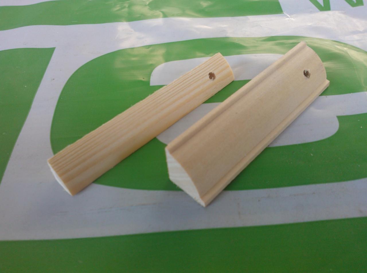 Dwie listwy drewniane o różnym profilu, z widocznymi otworami, leżą na zielono-białym tle. Listwa profilowana z zaokrągleniem. Surowe drewno.