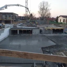 Wylewanie fundamentów pod budynek w Gołczy, widoczna świeżo wylana betonowa płyta, zbrojenie oraz ekipa budowlana w odblaskowych kamizelkach.