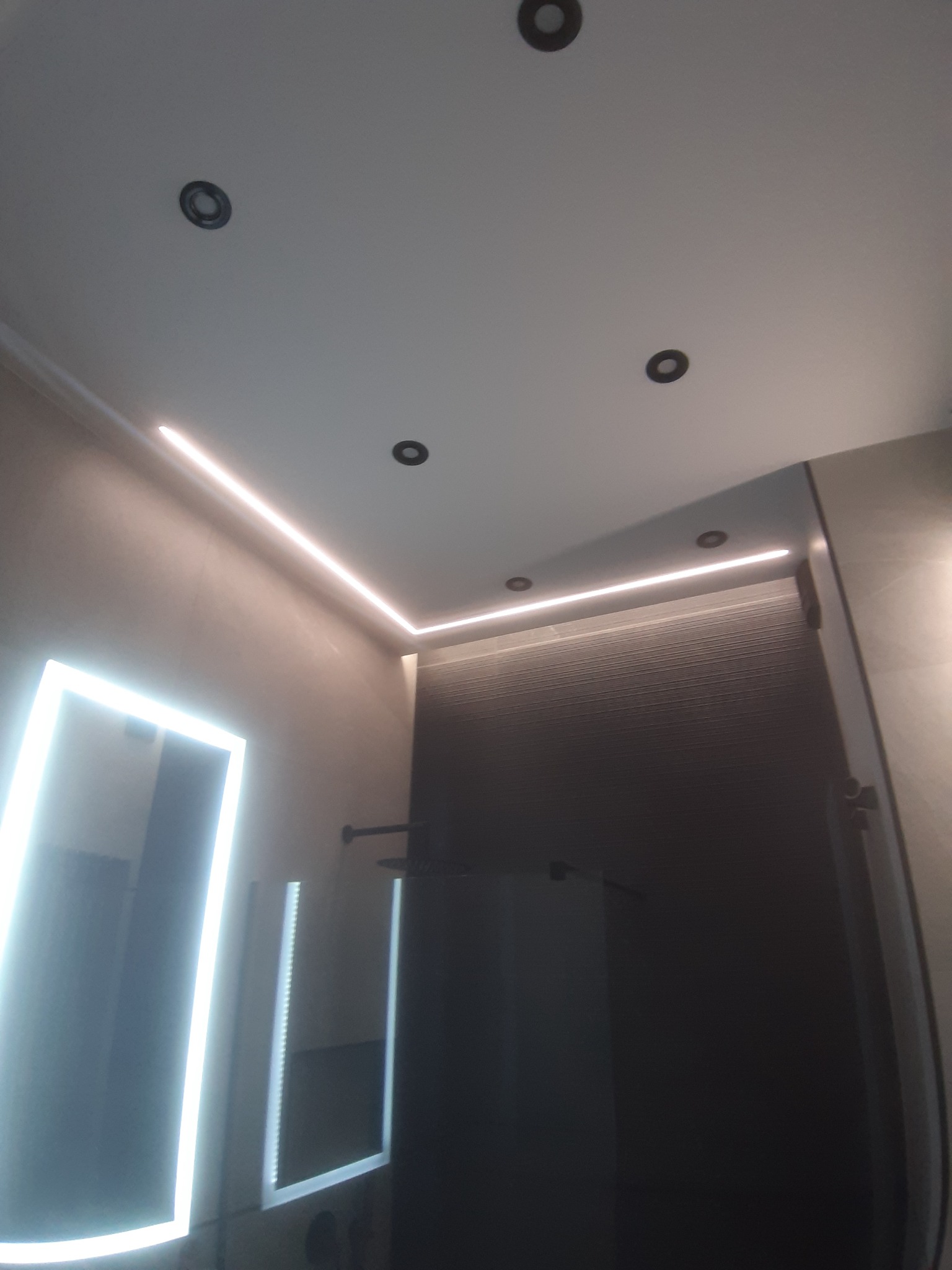 Nowoczesna łazienka z podświetlanym lustrem, oświetleniem LED podsufitowym i szarą ścianą z delikatną fakturą.