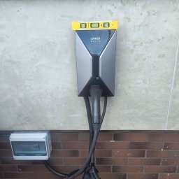 High Quality - Montaż ładowarki Anker Solix na teksturowanej ścianie z tynkiem i cegłą, z poziomicą na urządzeniu, skrzynką elektryczną i poprowadzonymi kablami.