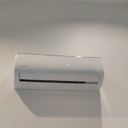 Paweł Stawicki Electric Energy - Nowoczesna, biała jednostka klimatyzatora ściennego marki Rotenso, zamontowana na gładkiej, białej ścianie, z wyraźnym cieniem pod urządzeniem, podkreślającym czystość instalacji.