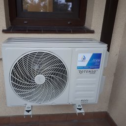 Paweł Stawicki Electric Energy - Nowo zamontowana zewnętrzna jednostka klimatyzacji Rotenso Roni Series na beżowej ścianie budynku w Babiaku, z widoczną naklejką firmy instalacyjnej, pod ciemnym oknem.