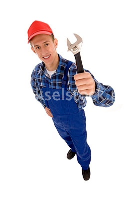 Uśmiechnięty hydraulik w niebieskim kombinezonie i czerwonej czapce, trzymający klucz nastawny, sfotografowany z dołu na białym tle.