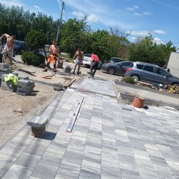 W Poziomie Bruk - Pracownicy układają nowoczesną, szaro-białą kostkę brukową o nieregularnym wzorze na podjeździe, z widocznymi narzędziami i częściowo ukończoną powierzchnią.