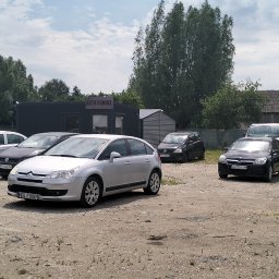 Skup Aut Elbląg El-Fura - Szutrowy plac z rzędem używanych samochodów, w tym srebrny Citroen C4 i czarny Opel Astra, przed budynkiem z napisem 'Auto Handel'.