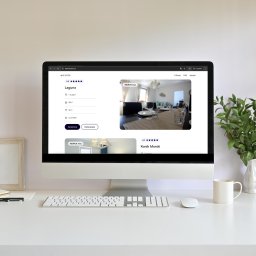 EnterSpace - Monitor wyświetlający stronę 'SEASIDE' z ofertą 'Laguna' (740PLN/noc) i zdjęciem jadalni. Na białym biurku klawiatura, mysz, zielona roślina i kubek.