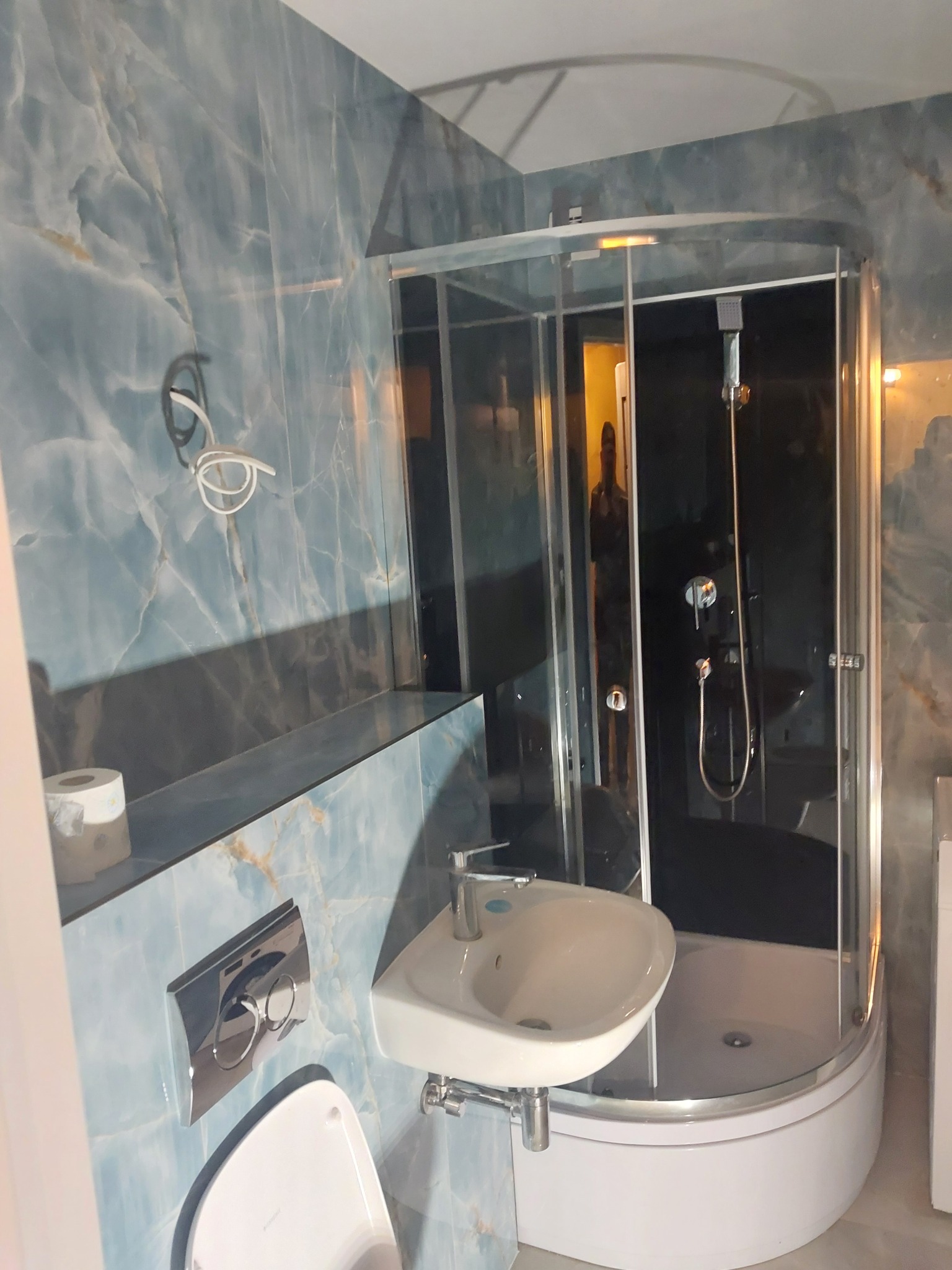 Wykończona łazienka z kabiną prysznicową, umywalką i toaletą. Ściany wyłożone płytkami imitującymi marmur w odcieniach błękitu. Nowoczesny design.