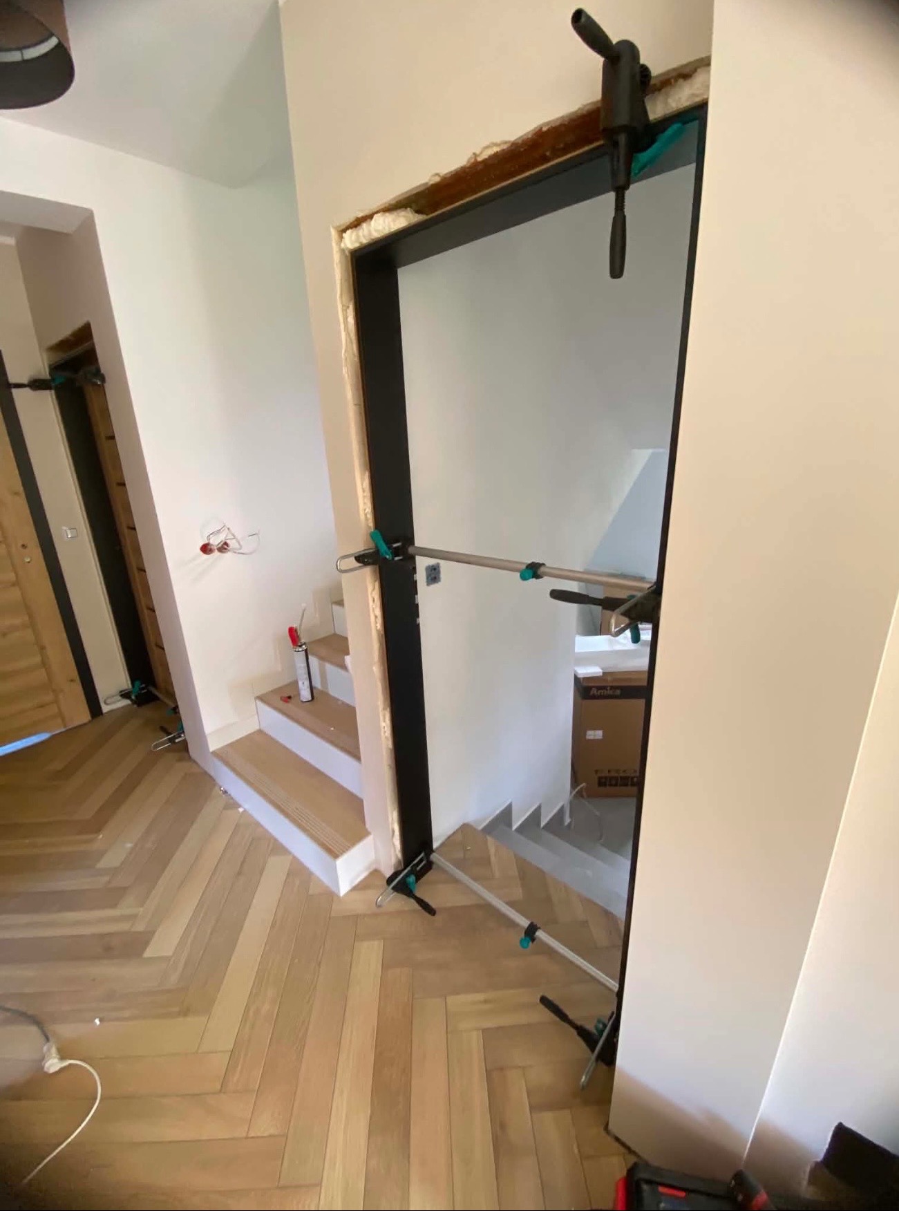 Wnętrze w trakcie prac wykończeniowych: drewniana podłoga w jodełkę, montowane ościeżnice drzwiowe z rozpórkami, schody i przewody elektryczne.