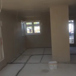 Wnętrze domu w stanie deweloperskim po nałożeniu tynków, widoczne instalacje podłogowe i wiadro po farbie.