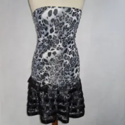 Sukienka koktajlowa bez ramiączek, z szaro-białym wzorem panterki na g&oacute;rze i czarnymi falbanami z koronki u dołu, prezentowana na manekinie.
