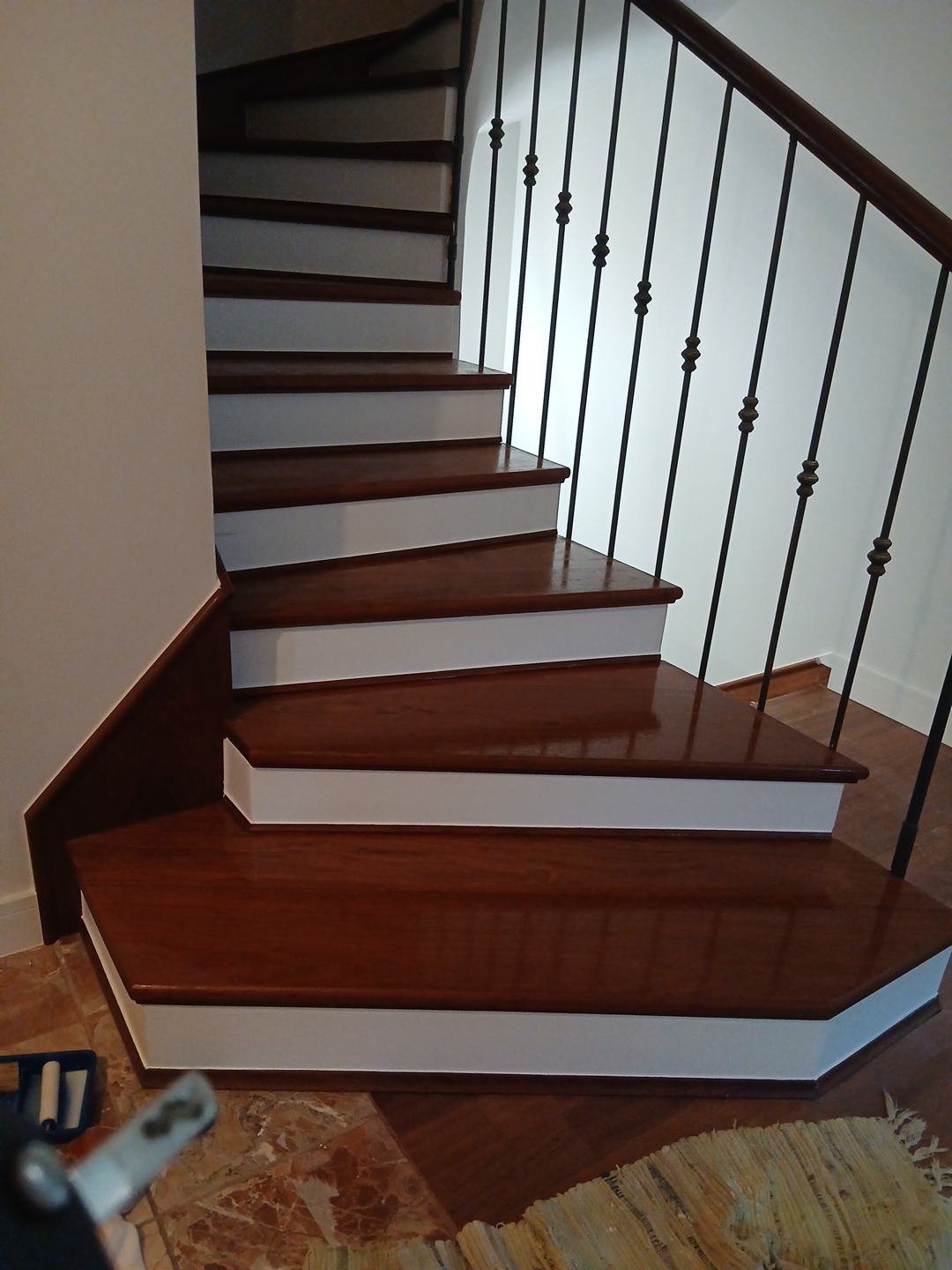 Odnowione drewniane schody z białymi podstopnicami i czarną balustradą. Widoczne ślady świeżego malowania. Częściowo widoczny wałek malarski.